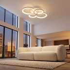 Ripple overlapping rings LED ceiling light mounted on the high ceiling of an open-plan living room with a cream boucle sofa and big windows