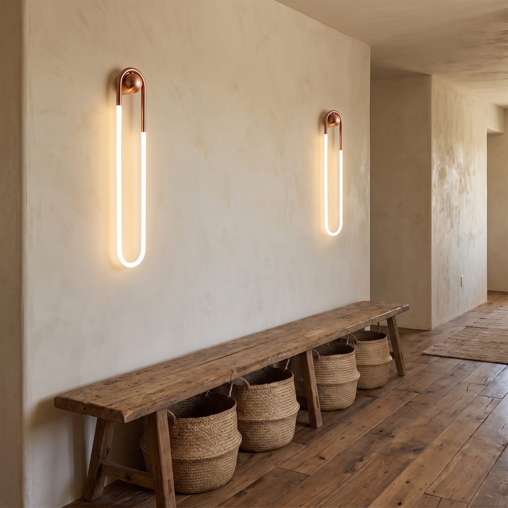 Coppa copper LED wall sconce a pair mounted on a limewashed wall along a rustic hallway with a wooden bench and woven baskets
