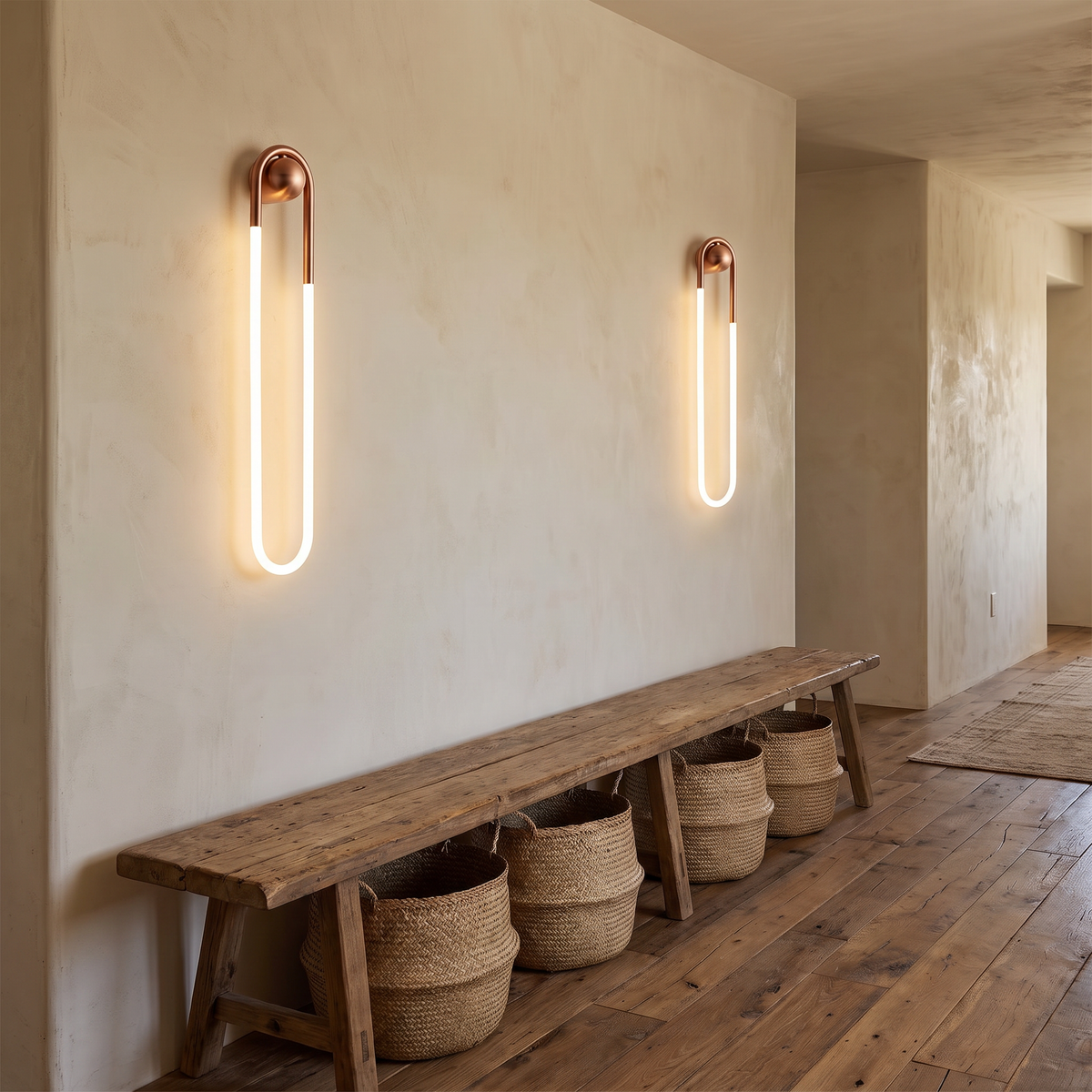 Coppa copper LED wall sconce a pair mounted on a limewashed wall along a rustic hallway with a wooden bench and woven baskets