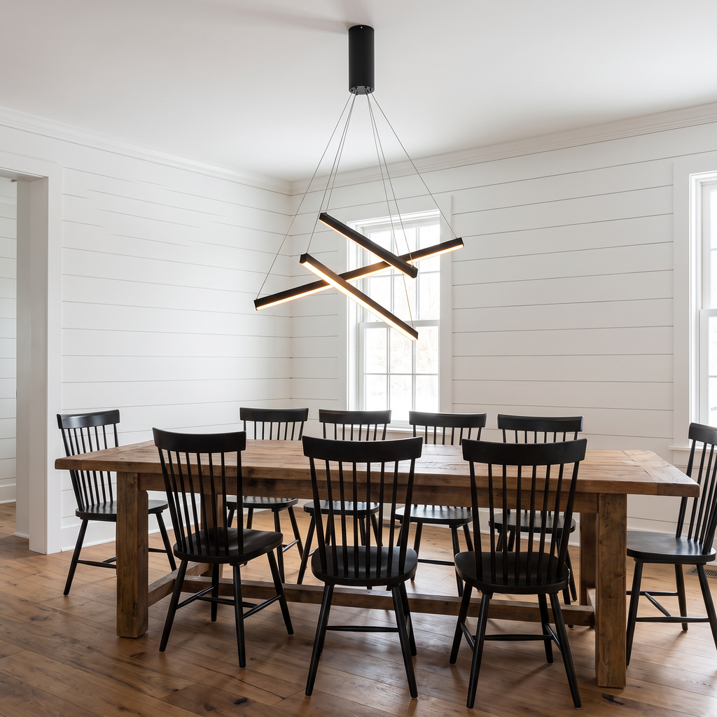 Criss crossed-bar linear LED chandelier hangs over a long dining table in a modern farmhouse dining room with white shiplap walls