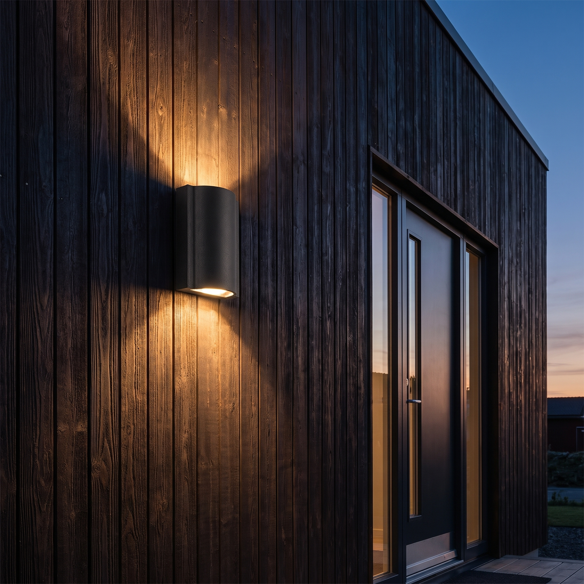 Rivo up-and-down outdoor wall light mounted on the dark wood-clad facade of a modern house beside the front door